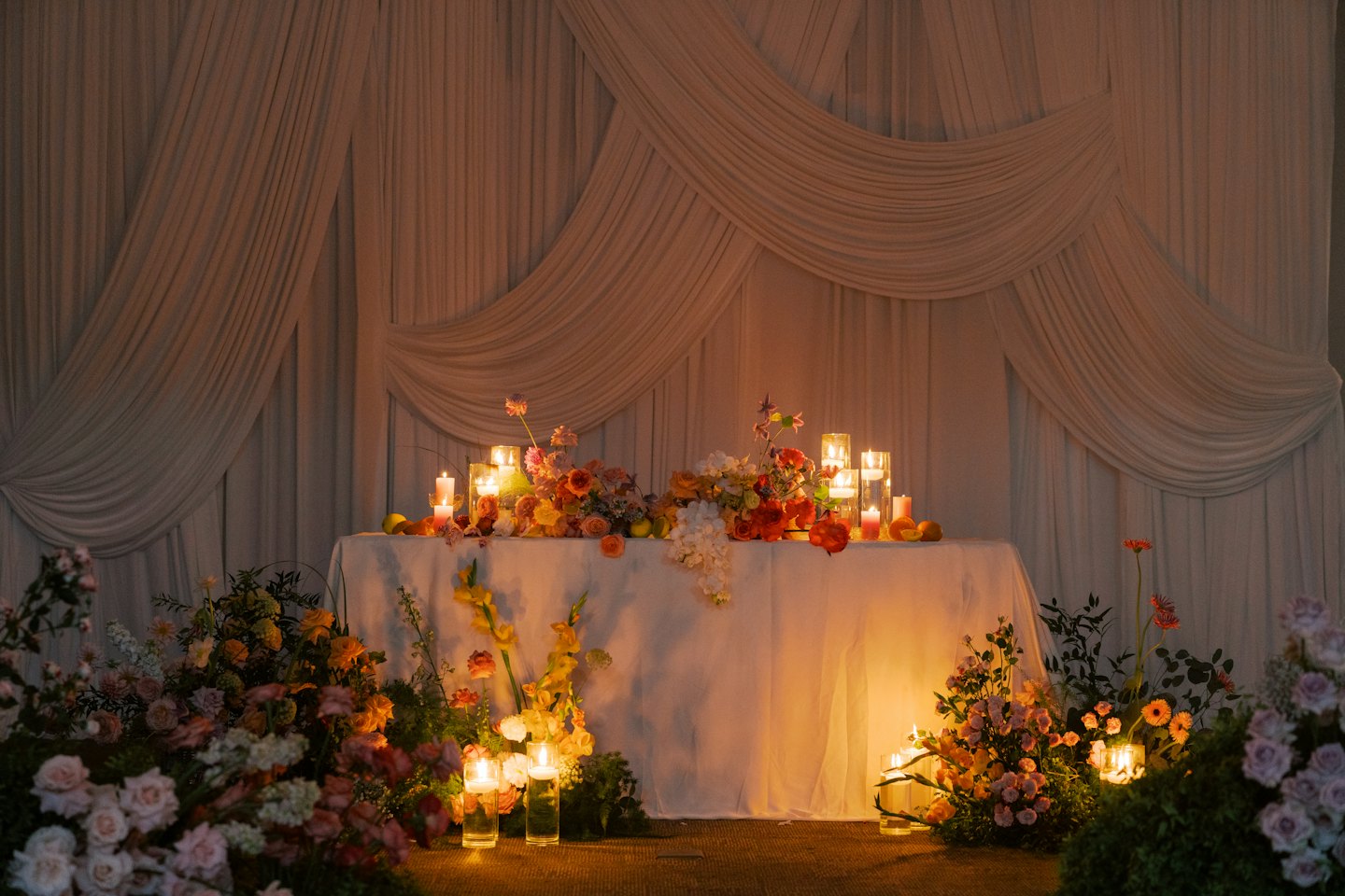 Bröllopsbord dekorerat med orange blomsterarrangemang och tända ljus.